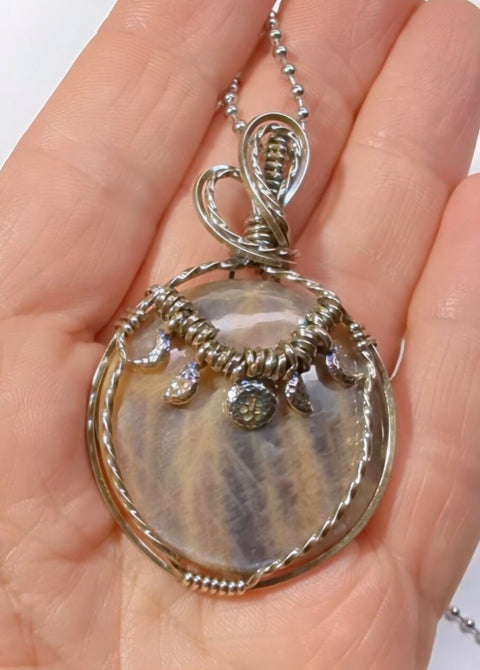 Black moonstone circular gemstones pendant with mesmerising blueish silver flash, set in a unique sterling silver twisted wire wrap setting and hanging from a stainless steel ball chain included for free in any size. This elegant gemstone comes in orange, black, browns, rust , greys and silver tones all mixed together like a dance of colours with a magnificent silver and blue flash from all directions when looked upon.